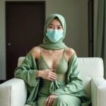 Woman in hijab and mask wearing green loungewear sits in a chair